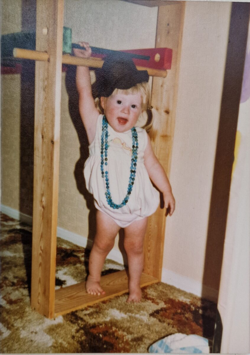 Smiling toddler with hat on and wearing an adult necklace happy to be the centre of attention