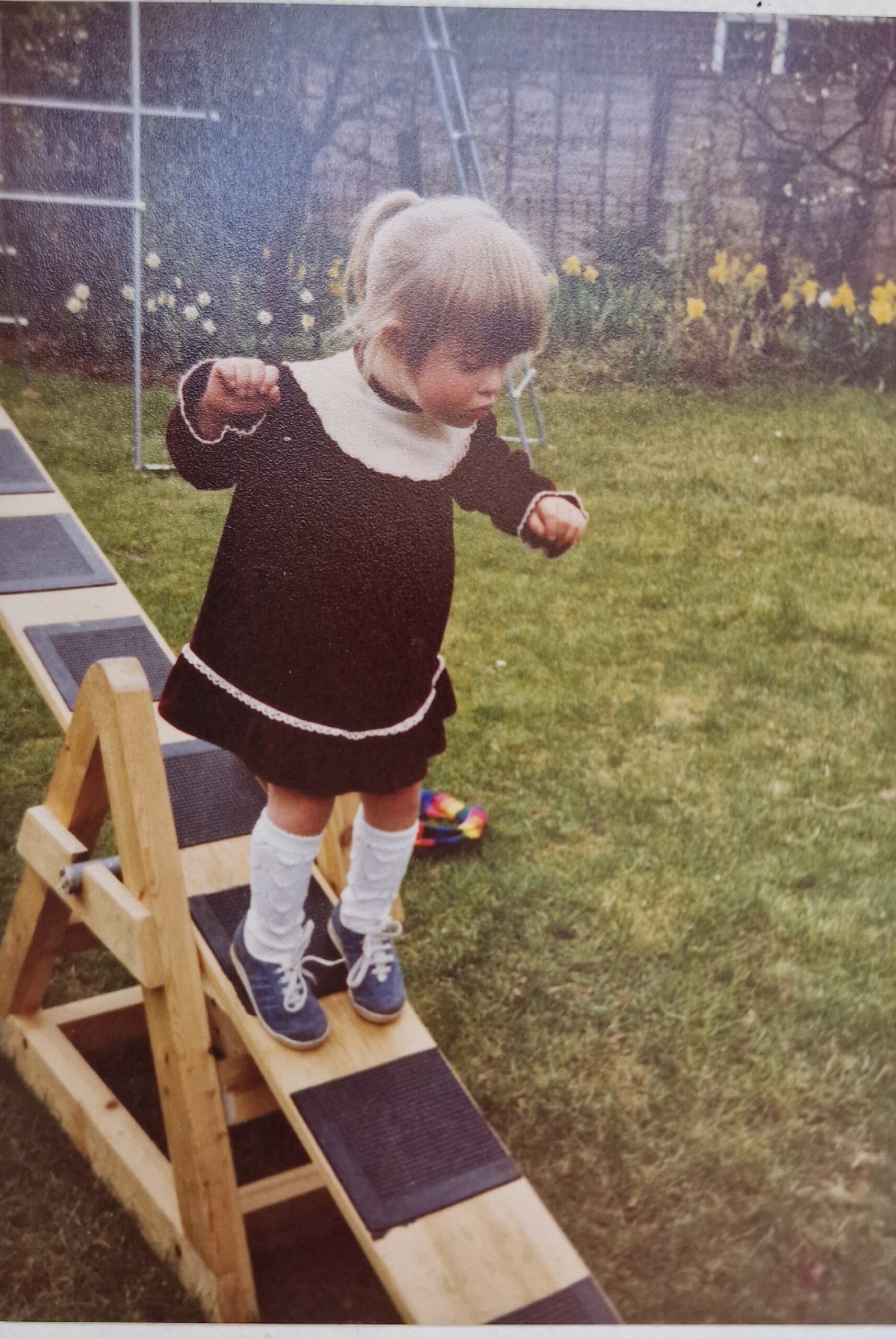 Little girl in dress and white socks walking down a seesaw
