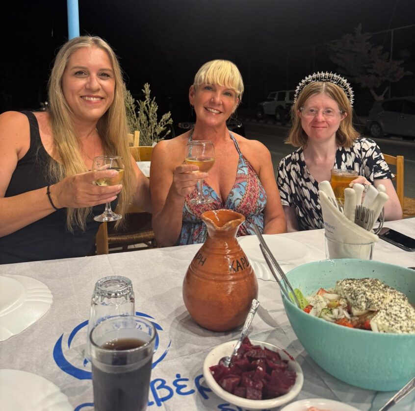 Three women smiling in summer dresses with food on table in front of them
