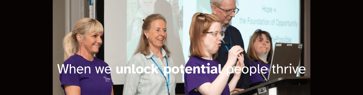 four people on stage one lady speaking into a microphone