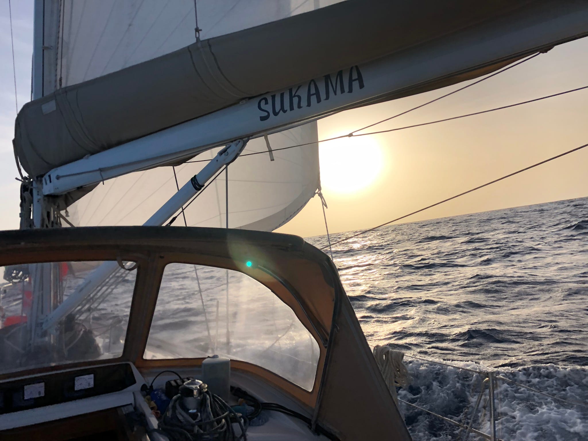 yacht on ocean with white sails up sailing on open sea towards sun that is setting