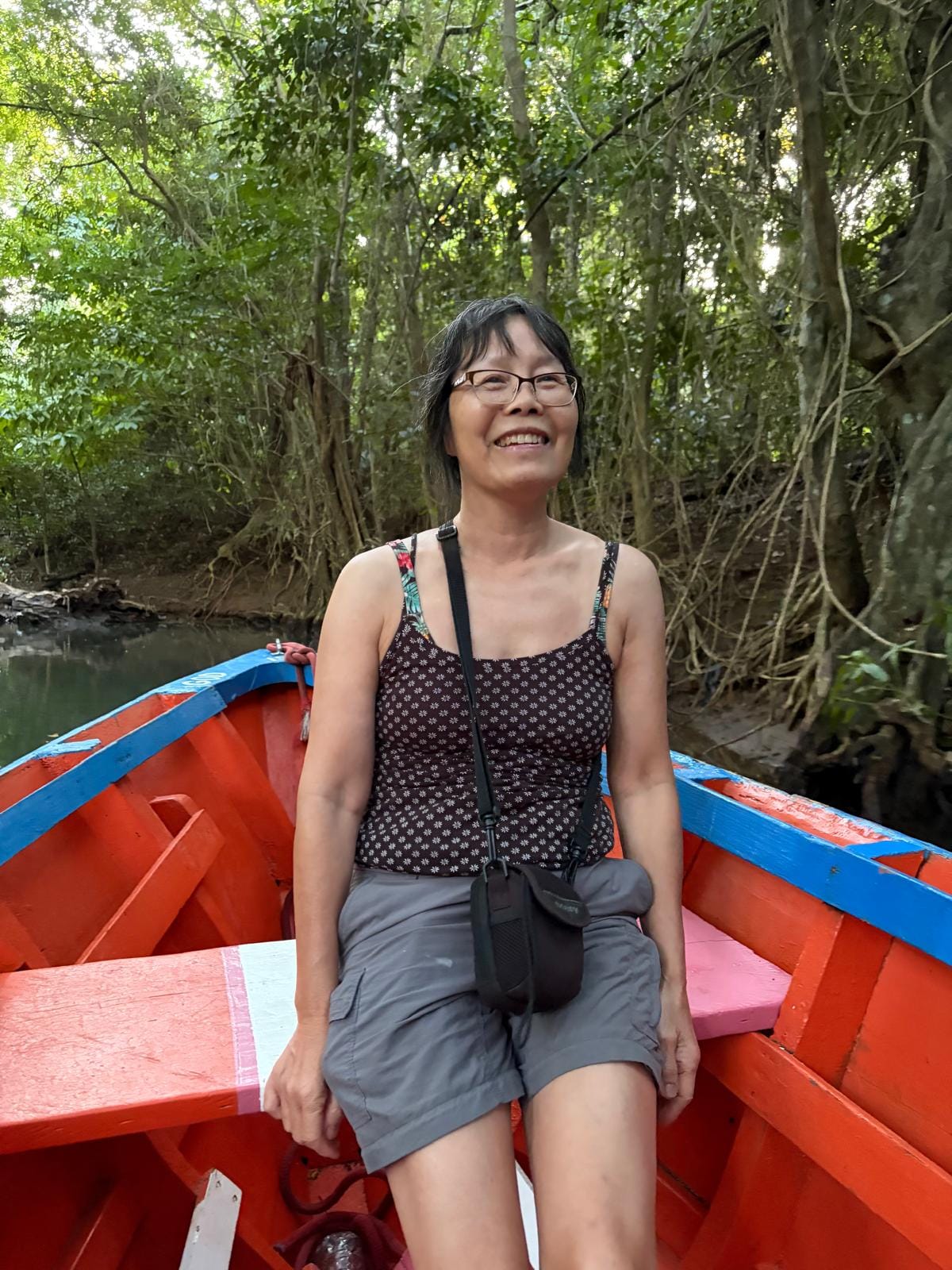 Lady in shorts and vest top on a red open rowing boat with lush green plants behind
