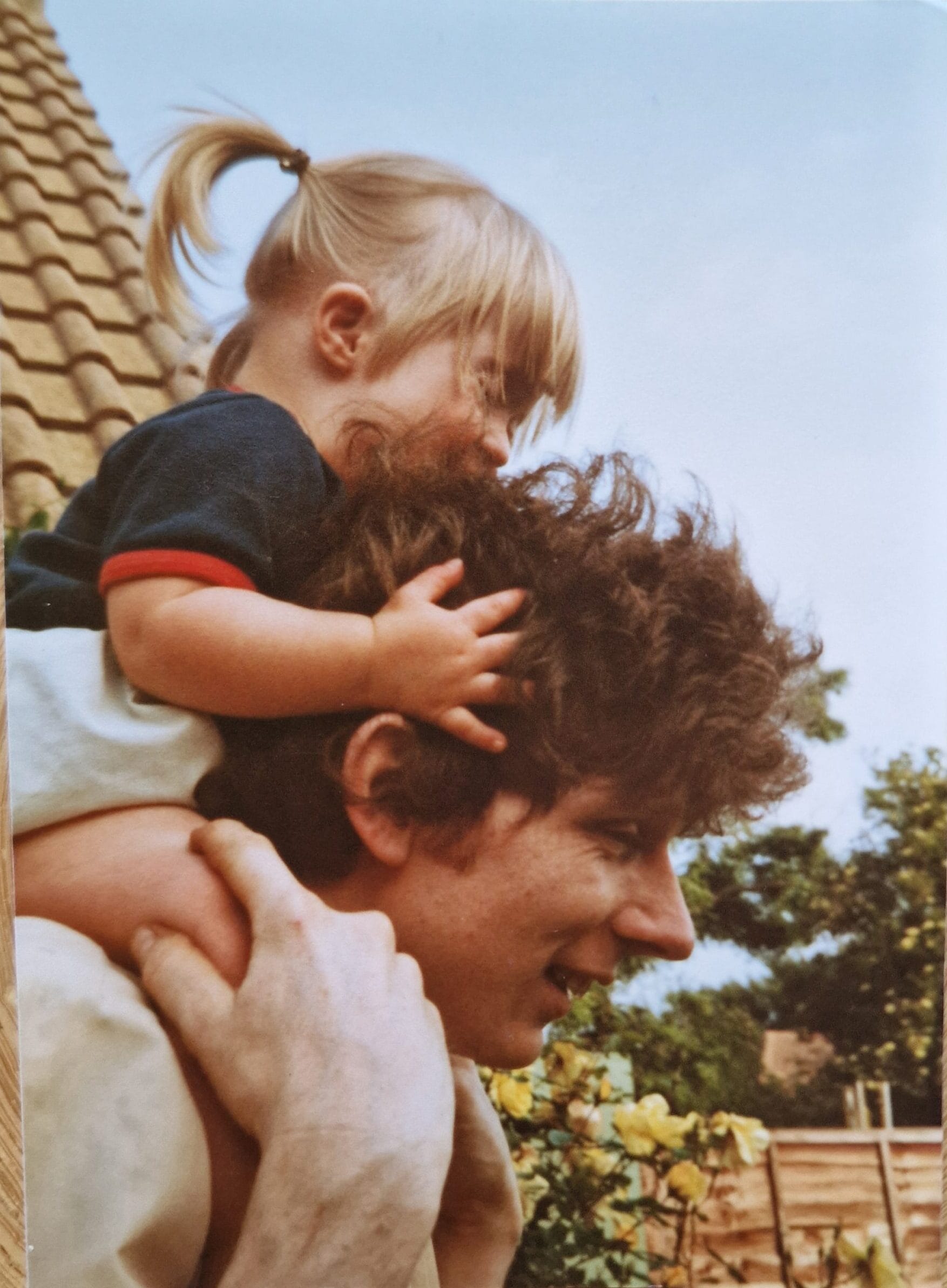 Little girl with hair in pigtail on mans shoulders in a garden