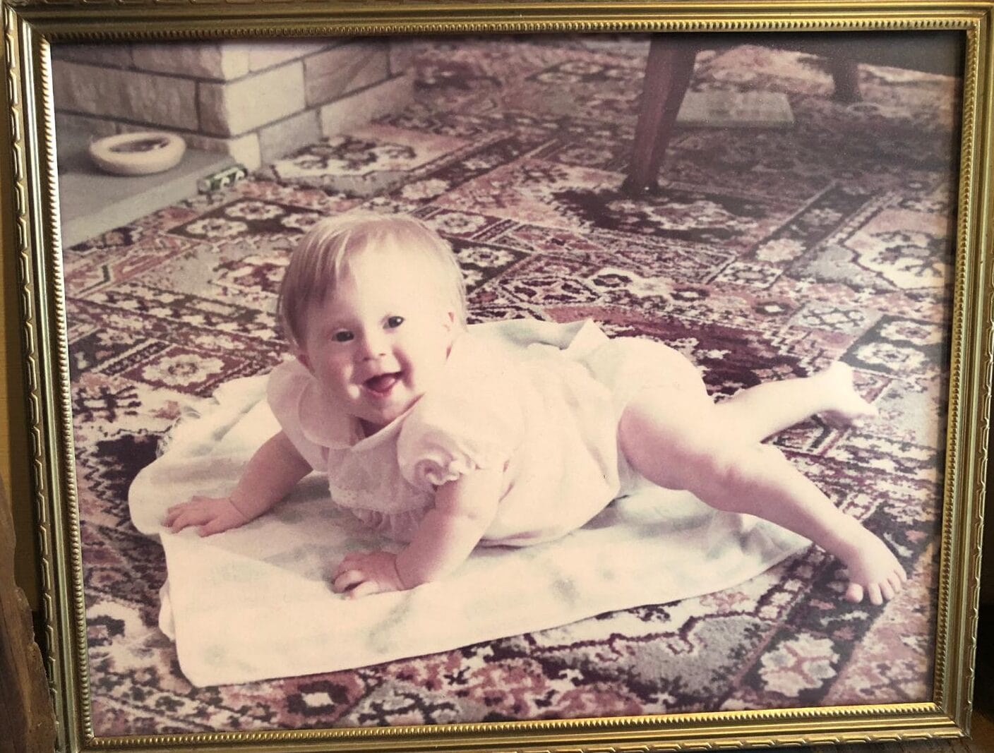 Baby kicking legs and pushing up on arms on mat on the floor smiling at camera