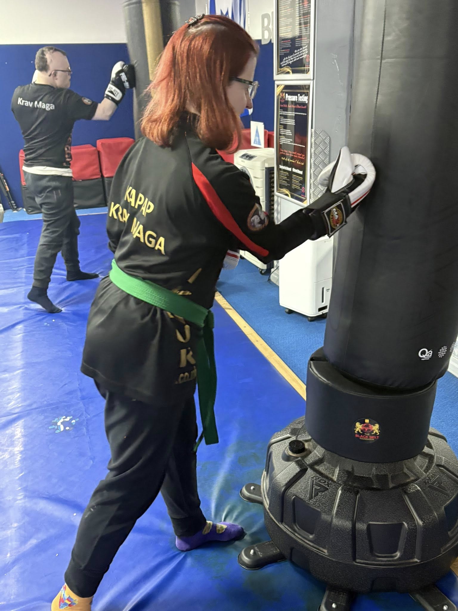 Jen punching a punch bag wearing martial arts clothing with a green belt