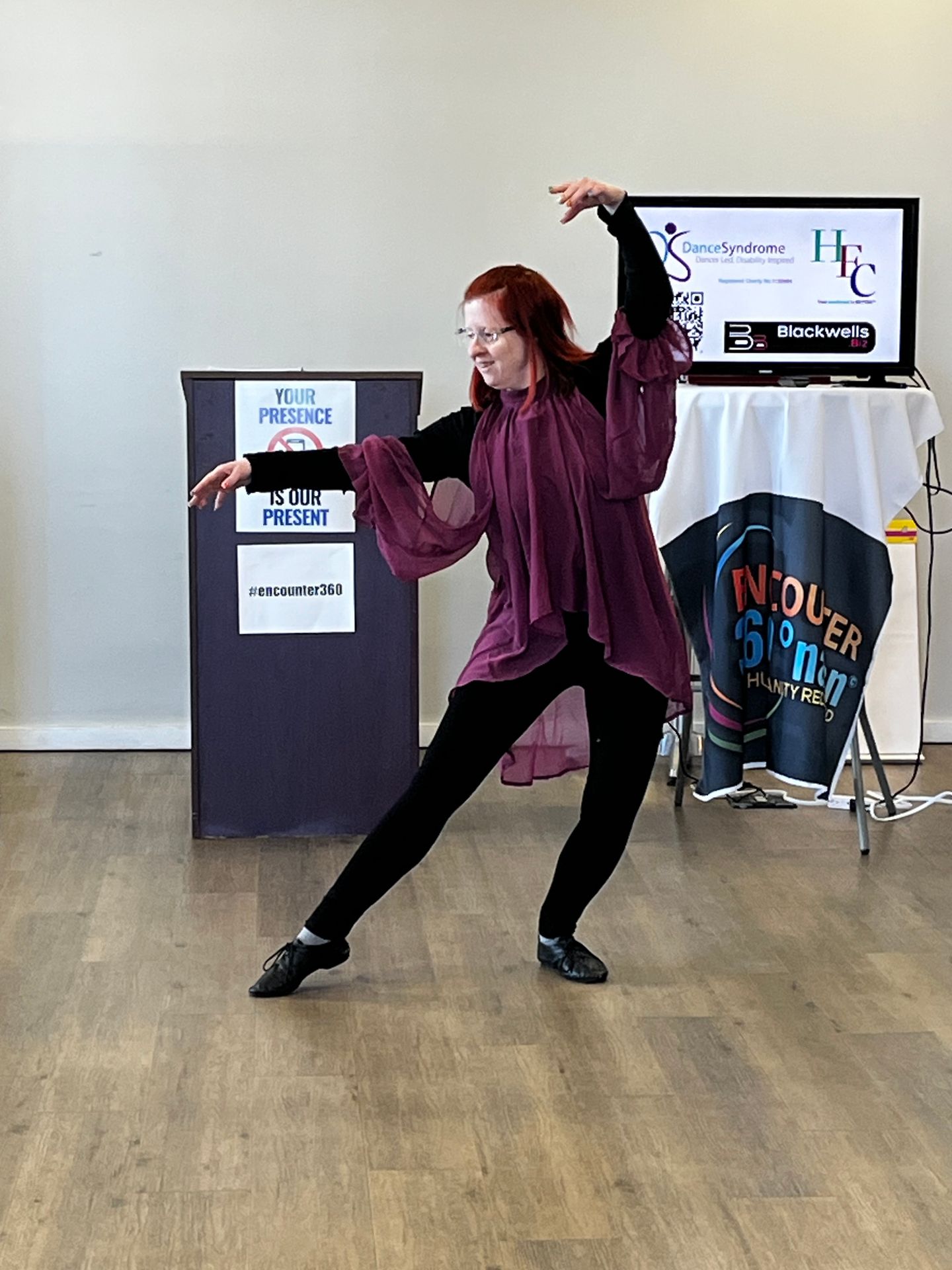 Jen Blackwell dancing with one leg pointed on the floor, one arm rounded over her head and the other arm straight out to the side.
