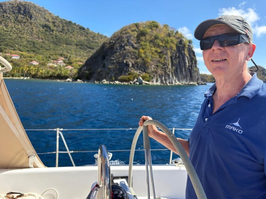 Malcolm at helm of yacht steering us to anchorage off island of Guadeloupe