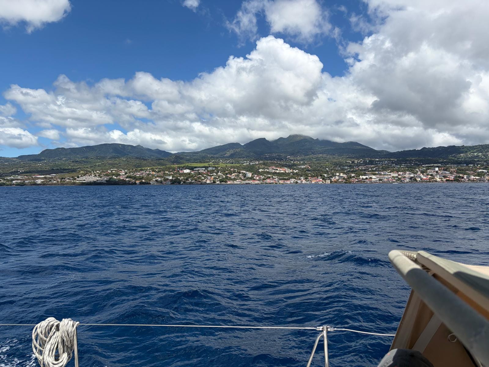 Looking at island from boat with white clouds over the green hills and town on the coast
