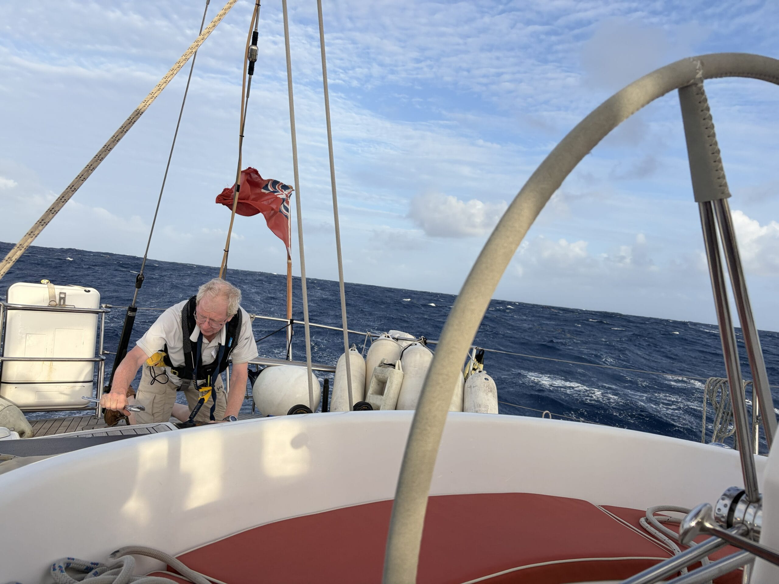 Man with life jacket on crawling on deck fixing something on yacht