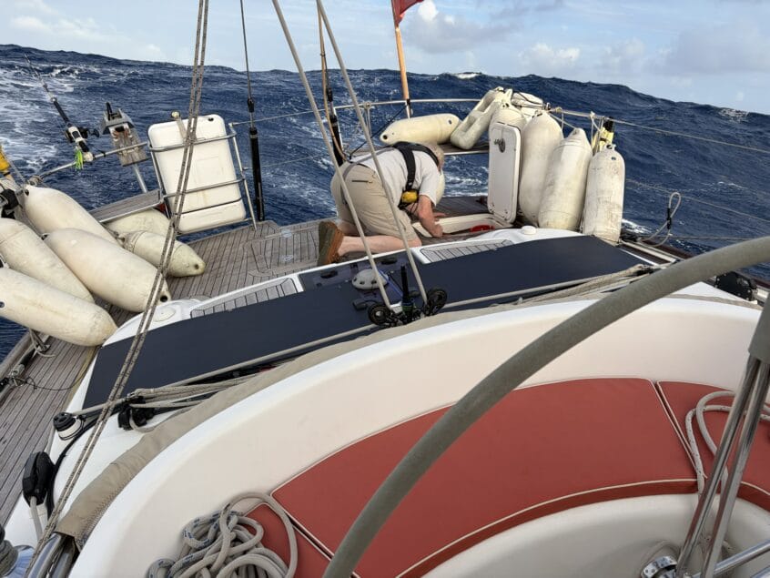Man wearing life jacket kneeling over a storage locker at the back of a yacht