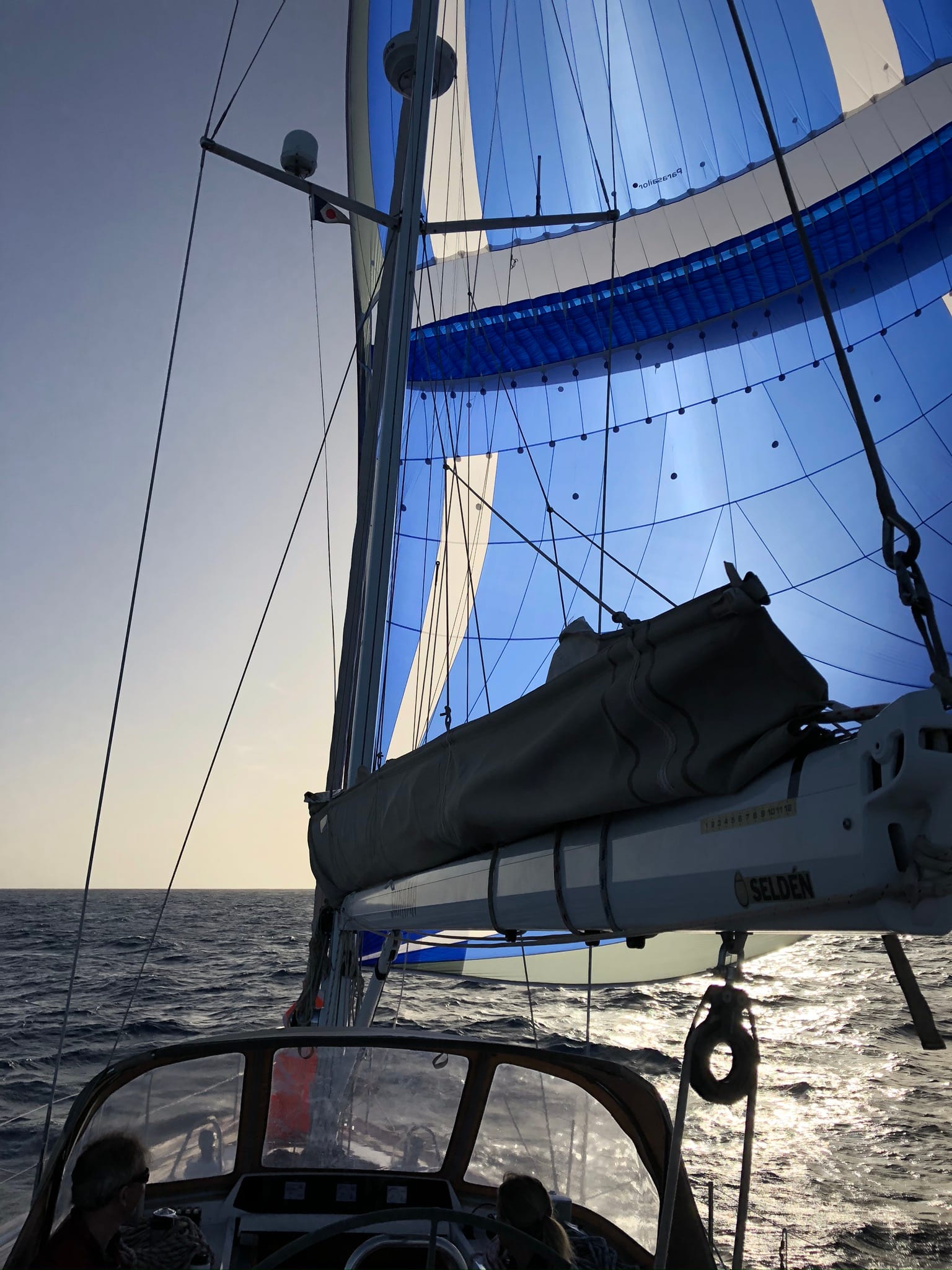 Blue parasail filled with wind heading towards the sun on a yacht