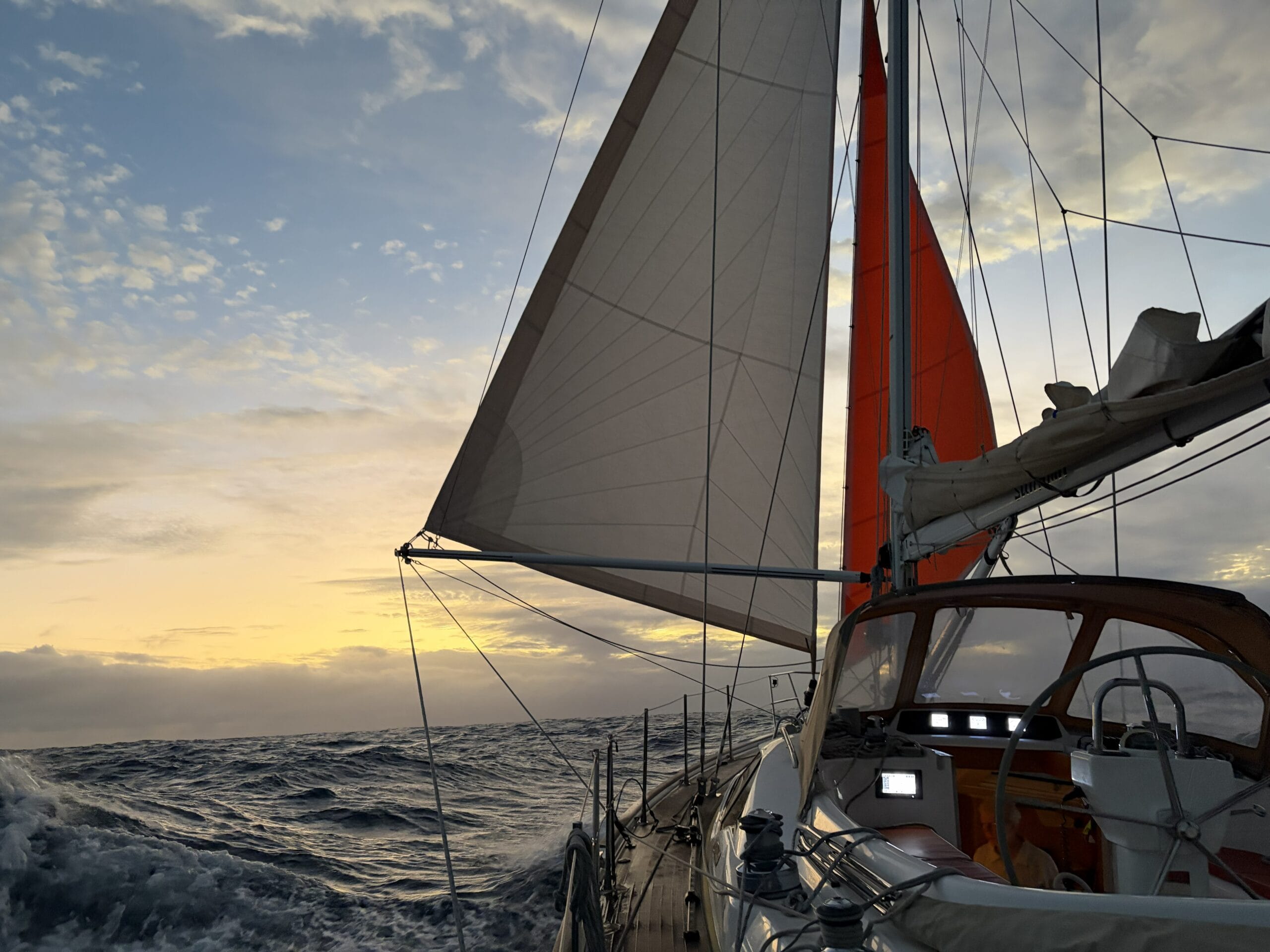 Yacht sailing in open sea towards sunset with sails both sides held out by a pole