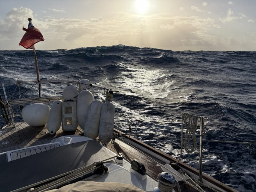 Looking to setting sun from back of yacht with waves rolling towards boat