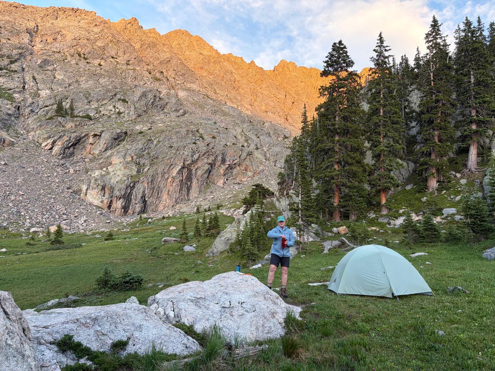 small hiking tent in clearing overlooking mountains as sun rises