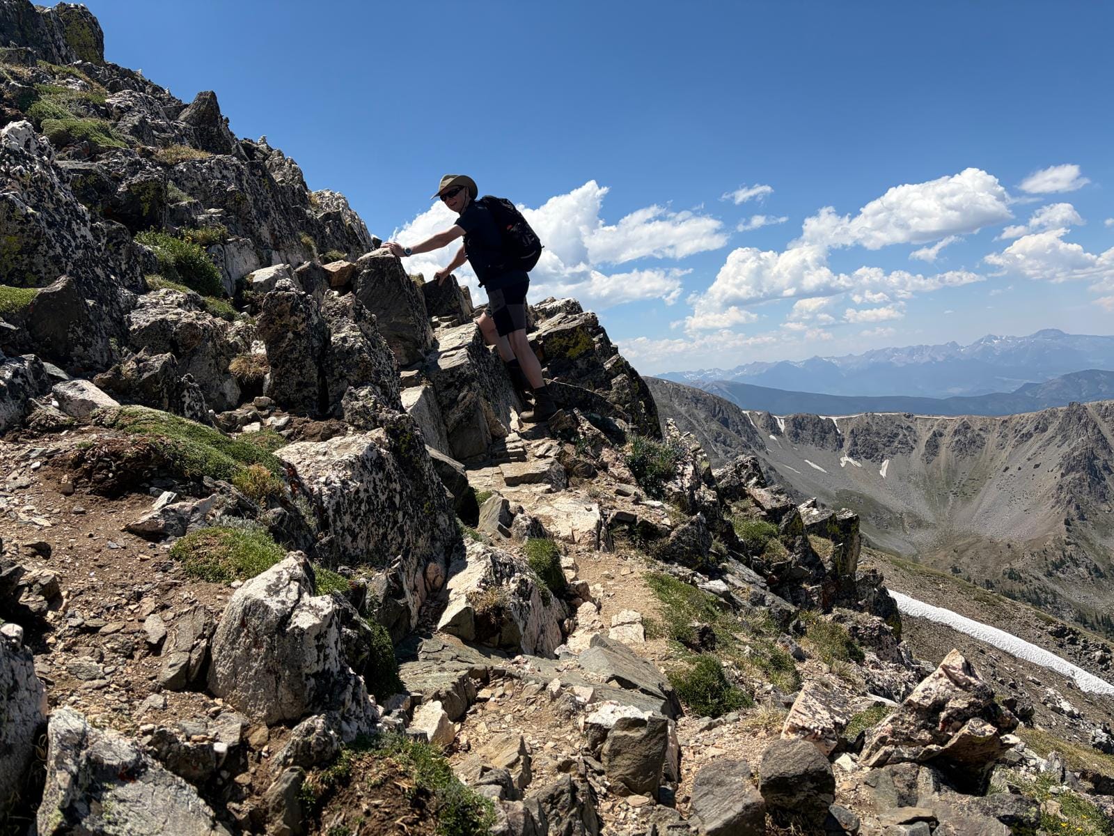 Man holding rocks on steep narrow path at top of mountain overlooking a wide expanse of Colorado