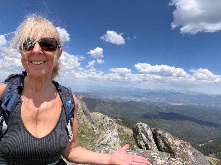 Sue wearing sunglasses and huge smile on face on top of the world at continental divide colorado