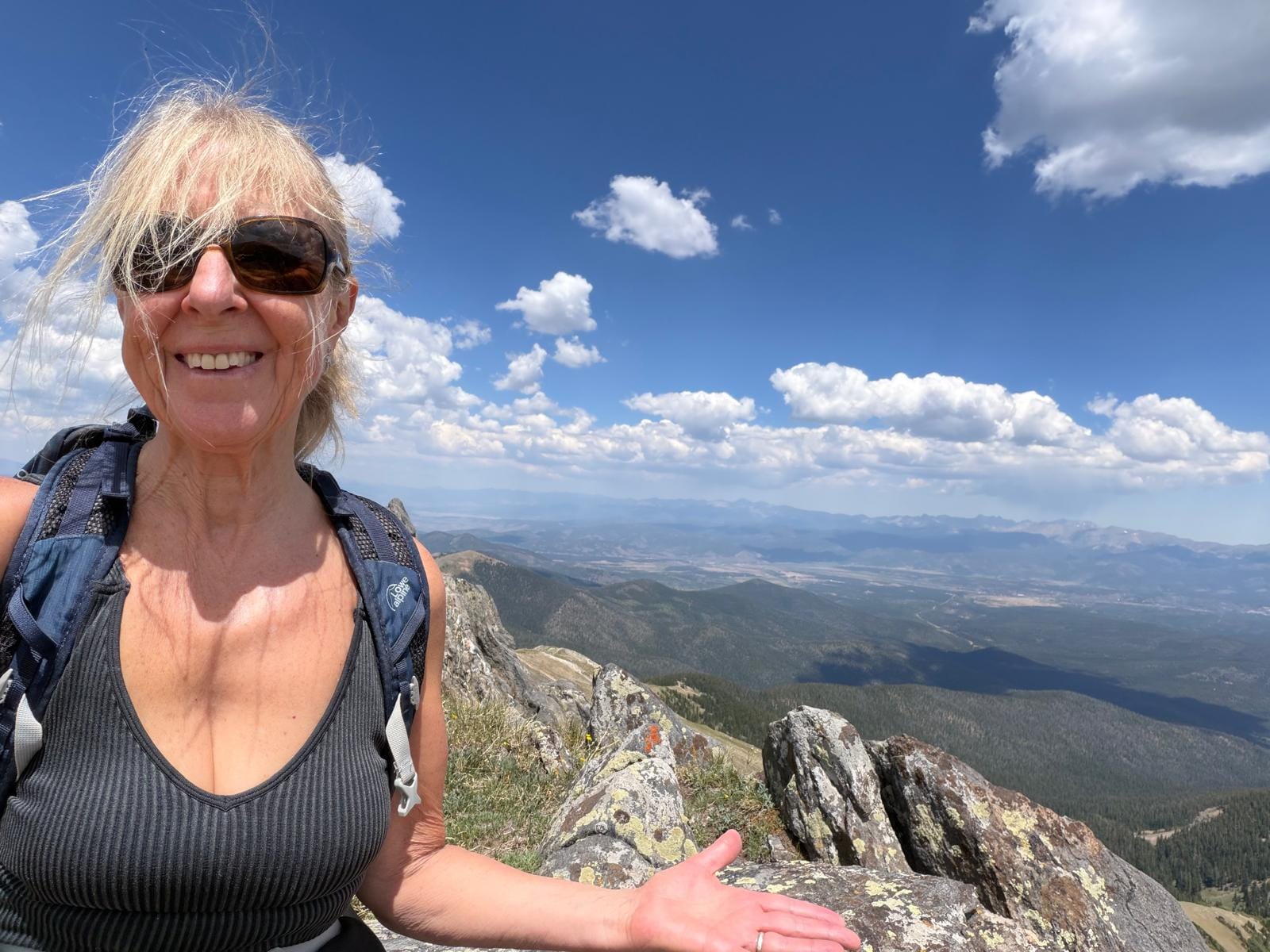 Sue wearing sunglasses and huge smile on face on top of the world at continental divide colorado
