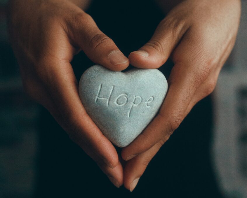 A heart shape pebble with HOPE inscribed held in hands shaped like a heart